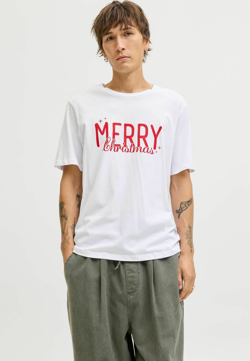 Witte katoenen t-shirt met opvallende rode tekst "MERRY Christmas". Korte mouwen, ronde hals, gedragen met losse lichtgroene broeken.