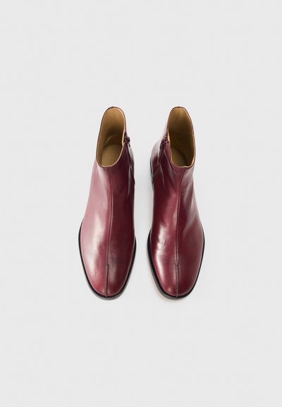 Burgundy läderankelstövlar med en slät finish, sidoglid, spetsig tå och kontrasterande svart sula. Enkl design och rena linjer.