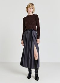 Brauner, strukturierter Strickpullover kombiniert mit einem dunkelgrauen, gefalteten Maxirock mit einem Oberschenkel hohen Schlitz und einem schwarzen Gürtel; getragen mit schwarzen Stiefeln.