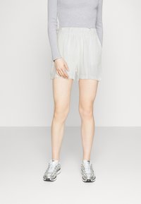 Pantaloni corti beige chiaro in tessuto testurizzato e stropicciato, con vita elasticizzata e tasche laterali, abbinati a scarpe da ginnastica argentate.