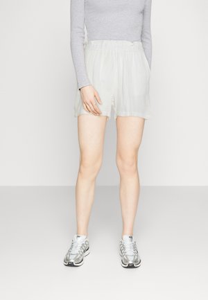 Lyse beige shorts i en teksturert, krøllet stoff, med elastisk midjebånd og sidelommer, kombineres med sølvfargede sneakers.