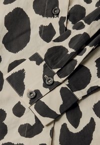 Leopardenmuster-Hemd in Schwarz und Beige, mit einem kragenförmigen Ausschnitt und geknöpften Ärmeln. Hergestellt aus einem weichen, glatten Stoff.