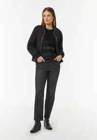 Schwarze Bomberjacke mit Reißverschluss, grünes gestreiftes Oberteil, dunkle Jeans und schwarze Stiefeletten, mit einer figurschmeichelnden Passform und glattem Stoff.