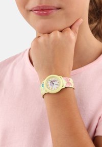 Gelbe Armbanduhr mit floralem Stoffarmband, rundem weißen Ziffernblatt, Zahlenanzeigen und dekorativen Schmetterlingsdetails.