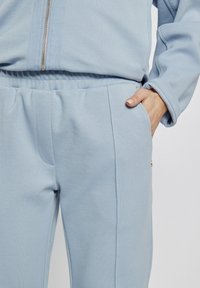 Jasnoniebieskie dresy wykonane z miękkiego materiału, z bocznymi kieszeniami i elastycznym paskiem w talii. Cechy to subtelne przeszycia oraz elegancki design.