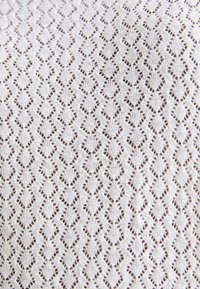 Tissu tricoté blanc avec motif ajouré en forme de losange répétitif formant des lignes verticales.