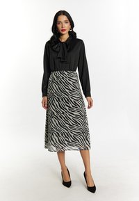 Blusa nera con dettaglio a fiocco, abbinata a una gonna fluente con stampa a zebra bianca e nera, completata da scarpe con tacco nere.
