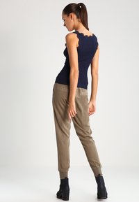 Débardeur côtelé navy avec un col festonné associé à un pantalon tapered beige clair et des bottines, mettant en valeur une silhouette ajustée.