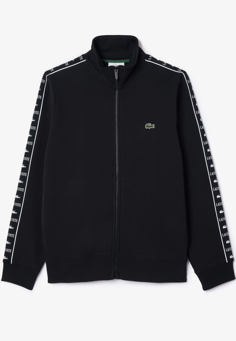 Schwarze Zip-up Sweatjacke mit hohem Kragen, ausgestattet mit grünem Lacoste-Logo und weißen Seitenstreifen mit wiederholtem Branding. Weicher, strukturierten Stoff.