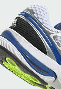 Chaussure de sport avec une tige argentée, un mesh noir et des accents bleus. Présente une semelle texturée avec des éléments néon verts et un design en couches.