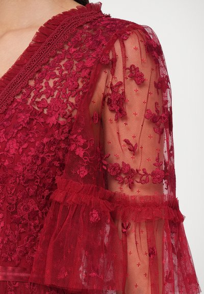 Burgundia pitsakate, millel on lilleline tikand, läbipaistvad varrukad, millel on rippuvad kummid, ja tekstuuriga kangas, millel on delikaatne mustriline viimistlus.