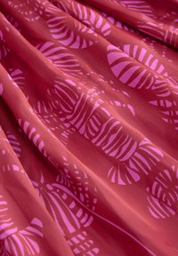 Tissu rouge avec une texture brillante, présentant un motif de feuilles abstraites roses et de rayures dans une disposition fluide.