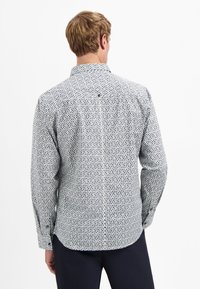 Wit long-sleeve shirt met een geometrisch marineblauw patroon. Beschikt over een button-down kraag en een enkele knoopdetail op de achterkant.