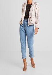 Blazer à carreaux avec des lignes rouges et beiges, blouse noire avec de grands points marron, jean taille haute bleu clair et escarpins à motif serpent.