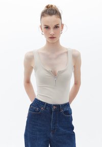 Beige body s zipovým předním zapínáním, širokými ramínky a přiléhavým střihem, spojený s modrými džíny s vysokým pasem.