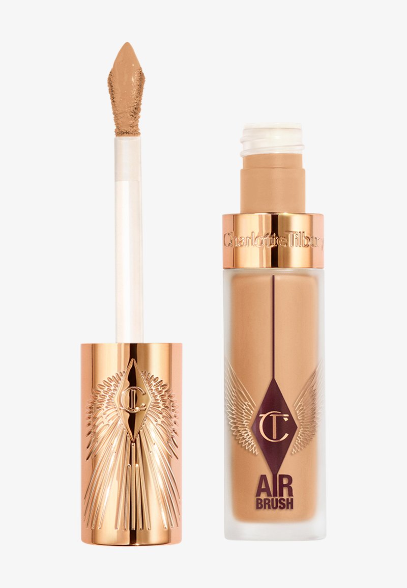 Fond de teint liquide dans un flacon transparent avec des accents dorés, présentant un design ailé et un bouchon pompe. Livré avec un applicateur en forme de mousse.