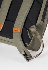 Zaino verde oliva con spallacci imbottiti, tessuto nero testurizzato e un accento in pelle beige con il logo "a/u". Presenta cerniere.