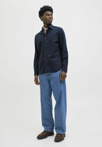 Navy knoopshirt met lange mouwen, gecombineerd met losse blauwe denim jeans en bruine laarzen. Heeft een recht-model ontwerp.