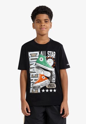 Garçon portant un t-shirt noir avec un graphique coloré de baskets Converse et le texte "All Star Converse Registered Trademark 1908."