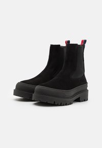 Botine negre din suedițe, cu o talpă din cauciuc groasă, panouri laterale elastice și tab-uri de tragere contrastante în roșu și albastru.