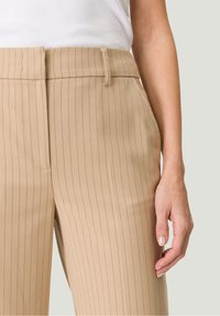 Pantalon beige à fines rayures avec une coupe ajustée, présentant une jambe droite, des poches latérales et une texture de tissu lisse.