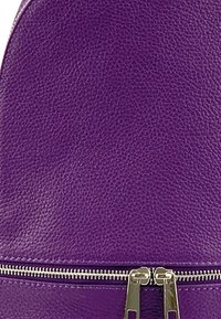 Sac à dos en cuir violet présentant une surface texturée, une forme arrondie et des accessoires en métal pour la fermeture éclair le long du bas.