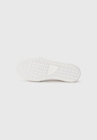 Fehér sneaker talp, texturált, zigzag mintával, kiemelkedő szélekkel és logó részletekkel. Simább felület, minimális ívvel az orrnál.