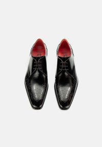 Schwarze Lederschuhe mit spitzen Zehen, ausgestattet mit roten Innensohlen und komplizierten geprägten Mustern auf dem Obermaterial. Traditionelles Schnürdesign.