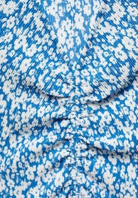 Tissu bleu à motif floral avec des fleurs blanches, présentant une texture froncée et un design à col en V. Matière douce et légère.