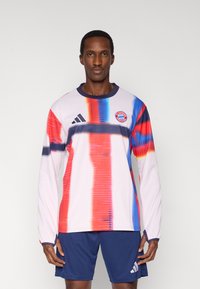 Rausva ilgomis rankovėmis futbolo marškinėliai su įvairiaspalvėmis vertikaliomis juostelėmis. Ant krūtinės yra „Adidas“ logotipas ir „Bayern“ Miuncheno emblema.