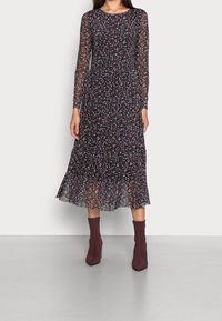 Šaty s dlouhým rukávem, černé květinové vzory, s volánovou sukní, průsvitný materiál a vícebarevné tečky; nošeny s burgundskými kotníkovými botami.