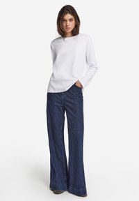 Witte lange mouwen overhemd gecombineerd met wijde donkerdenim jeans. De jeans hebben een afgewerkte zoom met een lichte versleten rand onderaan.