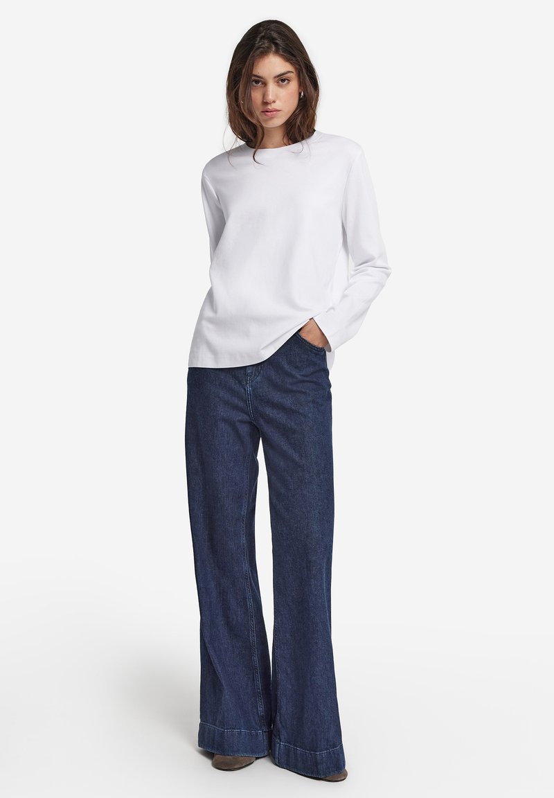 Witte lange mouwen overhemd gecombineerd met wijde donkerdenim jeans. De jeans hebben een afgewerkte zoom met een lichte versleten rand onderaan.