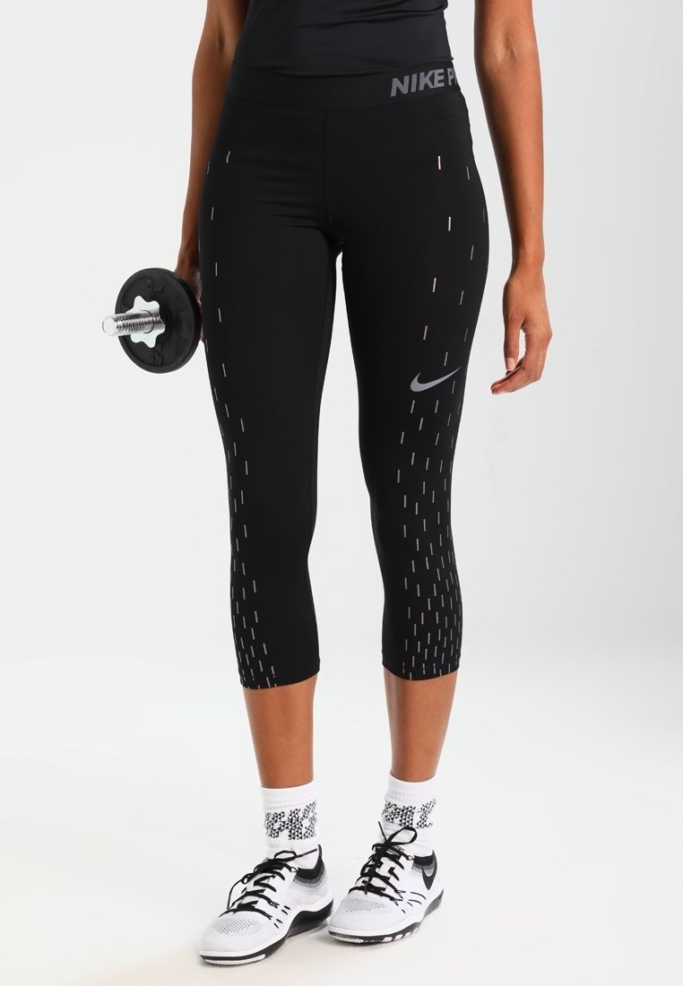 Leggings capri atletici neri con linee verticali riflettenti, caratterizzati da una alta vita e dal logo Nike. Abbinati a scarpe Nike bianche e a un manubrio.
