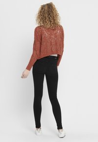 Stickad rostfärgad tröja med lös passform, med ett spetsmönster. Kombinerad med figursydda svarta jeans och vita sneakers.