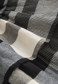 Czarna, biała i szara tkanina o różnorodnych wzorach w paski i kratkę, pokazująca szczegółowe zbliżenie splotu i fałd.