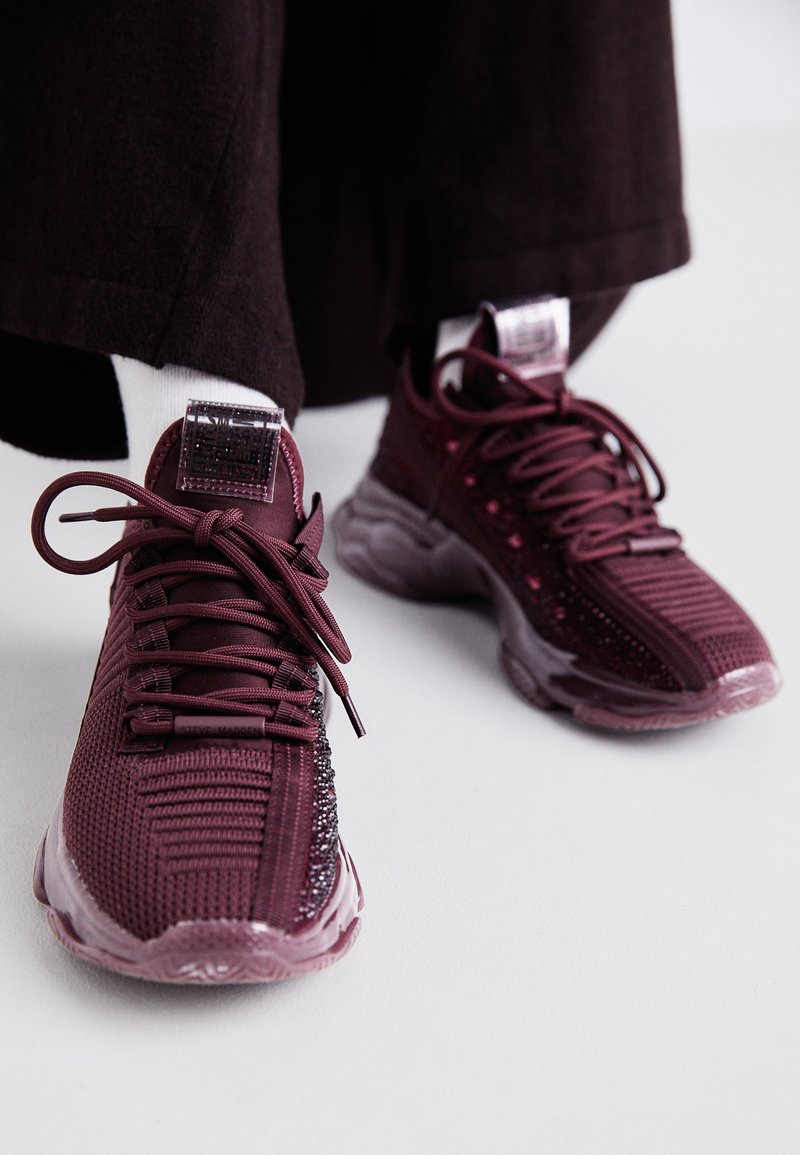 Baskets bordeaux avec tige en mesh, détails texturés, lacets ronds et semelle en caoutchouc transparent ; présente un logo sur la langue et le talon.