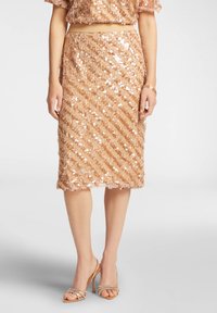 Gonna a matita in paillettes color rosa dorato chiaro. Caratterizzata da un motivo a righe verticali e una leggera lucentezza. Abbinata a sandali con tacco nudo e fasce.