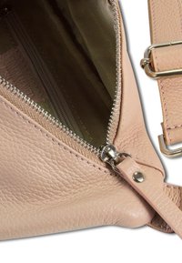 Lichtroze, gestructureerde leren tas die gedeeltelijk openzipper is, met een donkere stofvoering en een afneembare strap met een zilveren gesp.