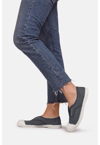 Baskets slip-on grises en toile avec des semelles en caoutchouc blanches et des accents de lacets à œillets, associées à un jean en denim bleu effiloché.