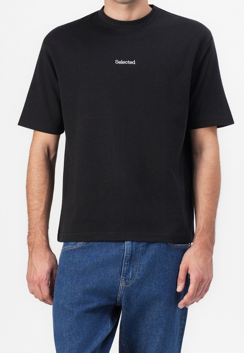 Black cotton t-shirt with short sleeves, round neckline, featuring "Selected" embroidered in white on the chest. Casual fit design.