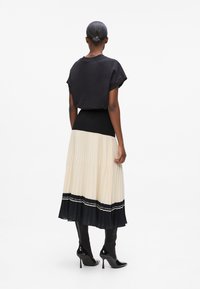 Black short-sleeve blouse with a round neckline paired with a pleated maxi skirt in cream and black, featuring decorative accents and fitted boots.