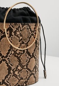 Sac seau à imprimé peau de serpent marron et noir avec une anse circulaire dorée et une fermeture à cordon en tissu noir.
