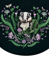 Badger otoczony zielonymi paprociami, różowymi i fioletowymi kwiatami oraz ćmami na ciemnym tle materiału, wyszyty szczegółowym haftem.