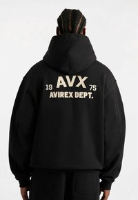 Felpa nera con cappuccio con testo ricamato "AVX 1975 AVIREX DEPT." sul retro. Presenta una vestibilità rilassata e polsini a costine.