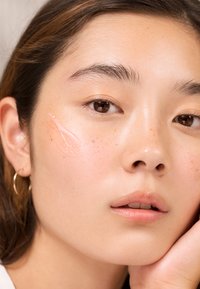 Primer plano de un rostro con piel suave y clara y ligeras pecas. Se ha aplicado un gel translúcido en la mejilla. El cabello es oscuro y ondulado.