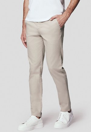 Beżowe chinosy slim fit z gładkiego materiału bawełnianego, z bocznymi kieszeniami i minimalistycznym wzornictwem, zestawione z białymi sneakersami.