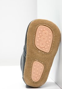 Svart lädersula med beige mockadetaljer, med ett prickigt gummigreppmönster och rundad form. Minimalistisk design, platt profil.