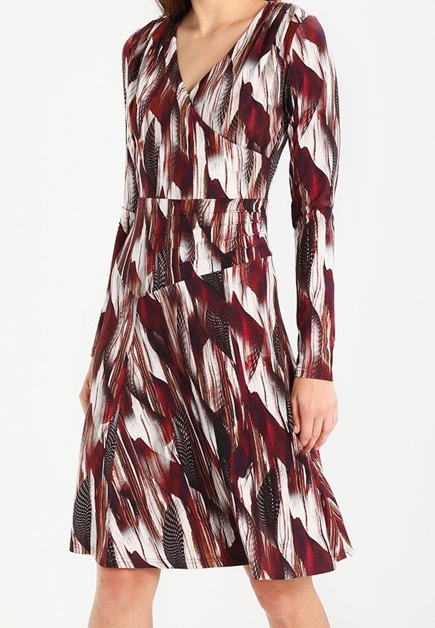 Femme portant une robe mi-longue à manches longues avec un motif abstrait de plumes rouges, noires et blanches et un décolleté en V.