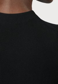 Närbild av ett svart ribbat stickat plagg som framhäver texturen och halslinjen. Fokus ligger på tygets mönster och form.